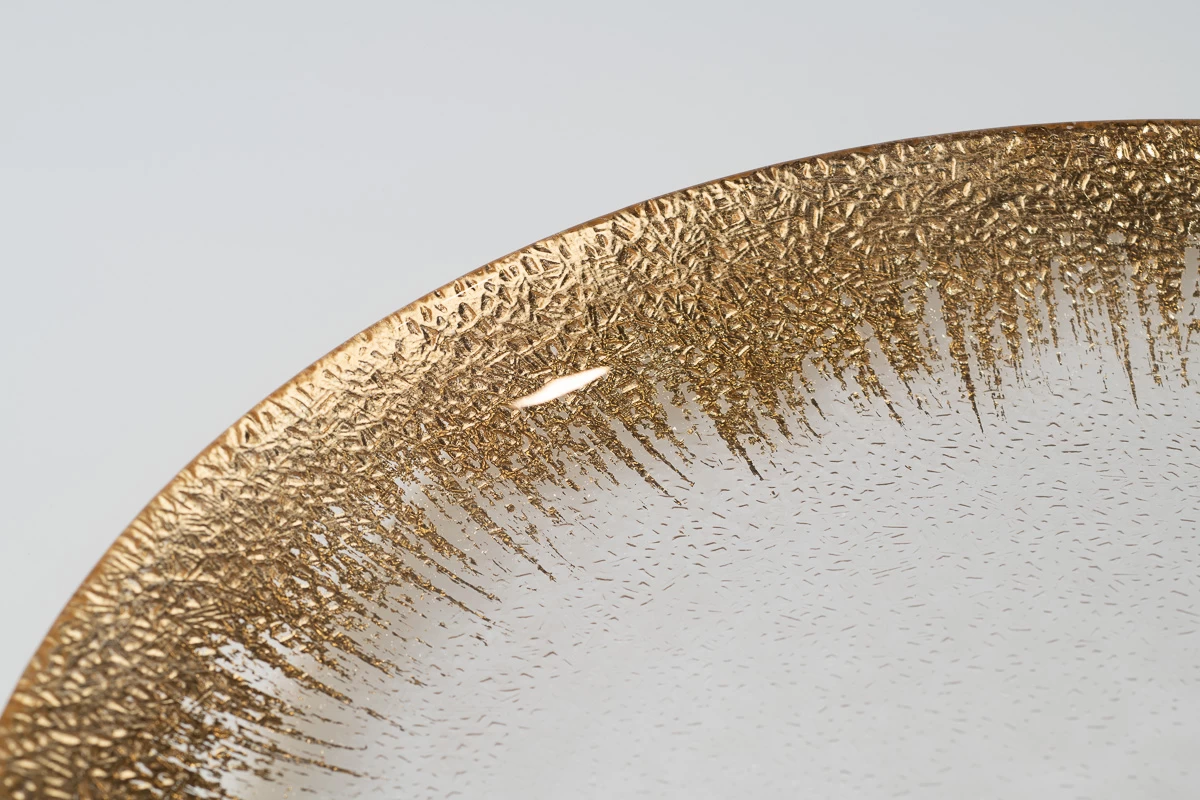 צילום תקריב על שוליים של צלחת זכוכית דקורטיבית עם עיטור זהב. צילום מקרוב של שולי הצלחת, המציג את הטקסטורה העדינה ואת הגימור היוקרתי. תאורת סטודיו מקצועית.