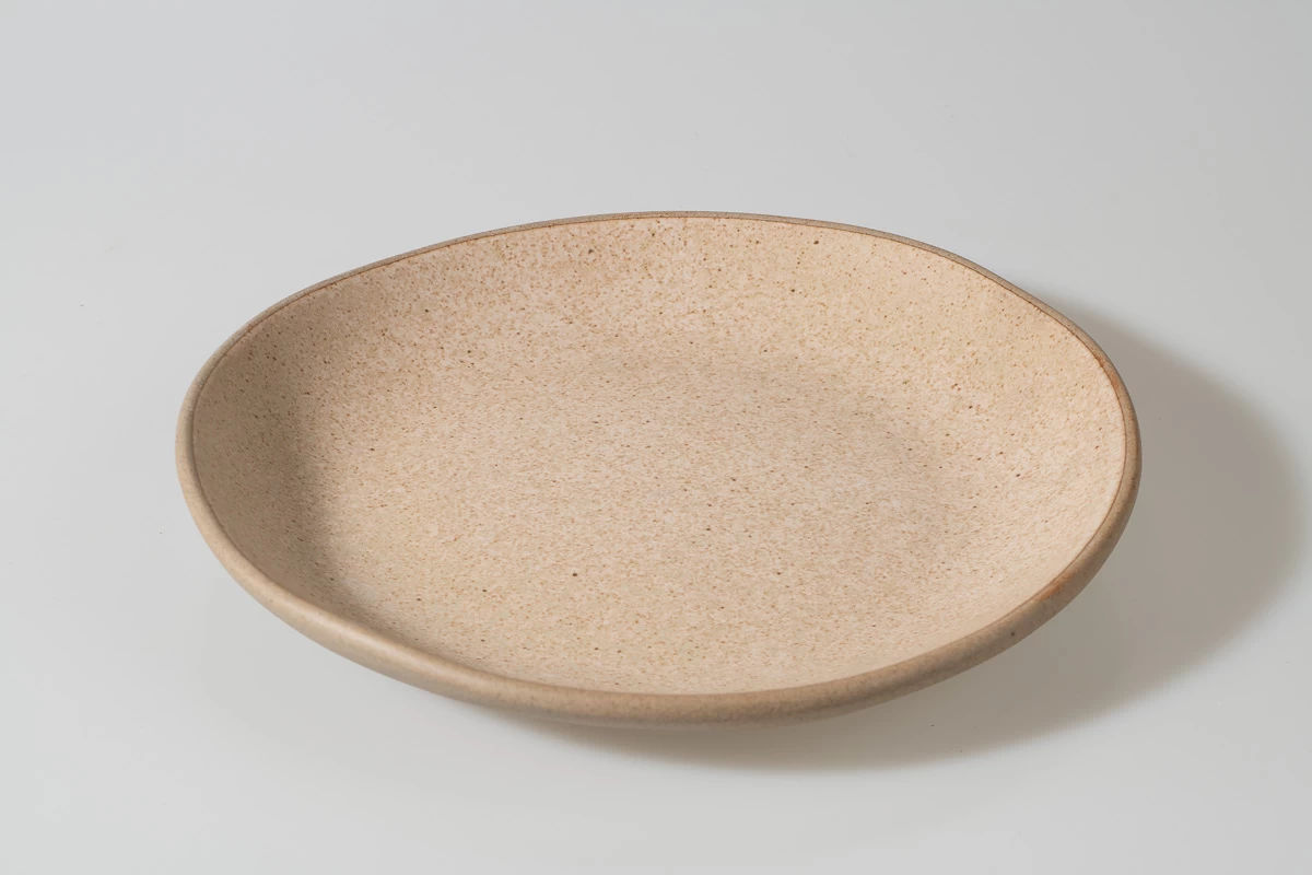 צלחת קרמיקה בז' אובלית מצולמת בסטודיו. צלחת מעוצבת בעבודת יד, מתאימה לעיצוב שולחן מודרני. צילום מוצר מקצועי לאתר מכירות.